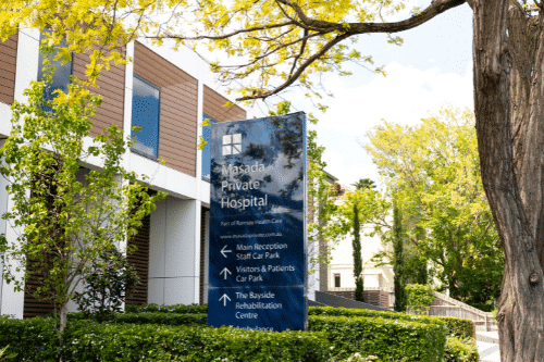 Exterior view of Masada Private Hospital in St Kilda East, Melbourne, surrounded by trees and signage directing visitors to hospital services including rehabilitation and ENT care.