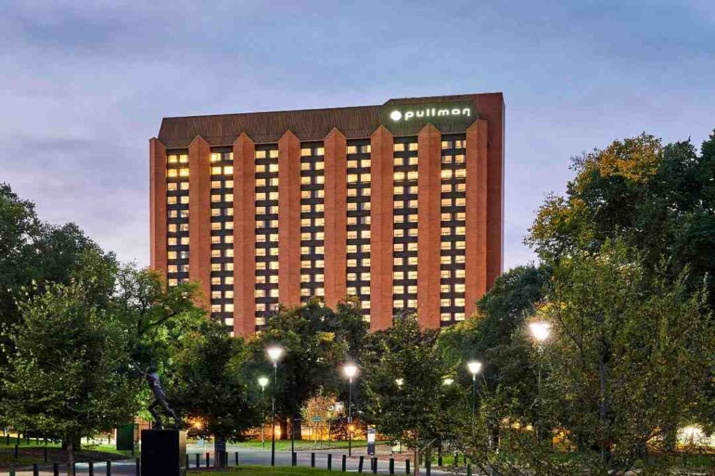 Front view of Pullman Melbourne On The Park hotel at 192 Wellington Parade, East Melbourne, a luxury high-rise accommodation with illuminated windows, located beside Fitzroy Gardens and overlooking the MCG and Rod Laver Arena.