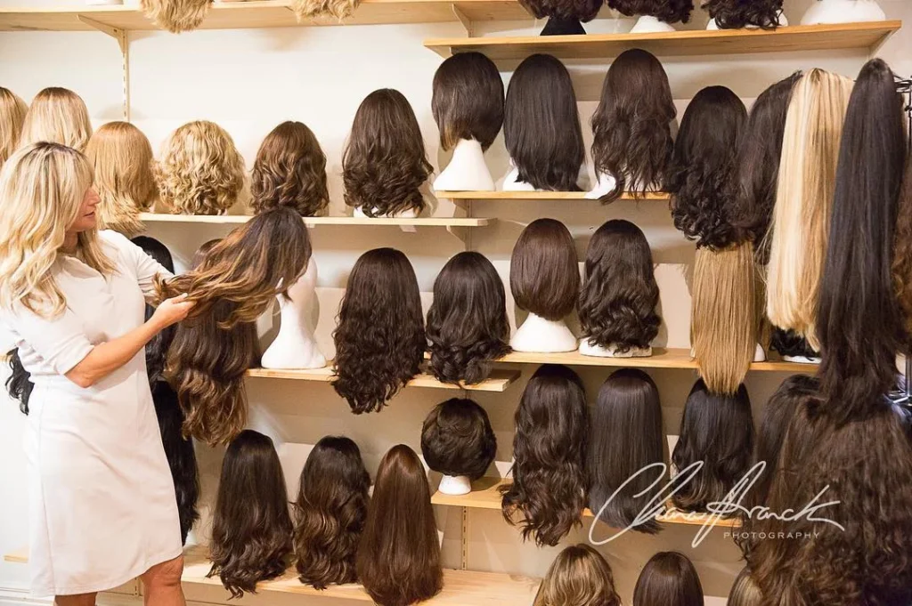 Display of premium European hair wigs at Wigs by Eva in St Kilda, Melbourne, featuring a variety of long, natural-looking wigs on mannequin heads and a stylist showcasing a highlighted brunette wig.